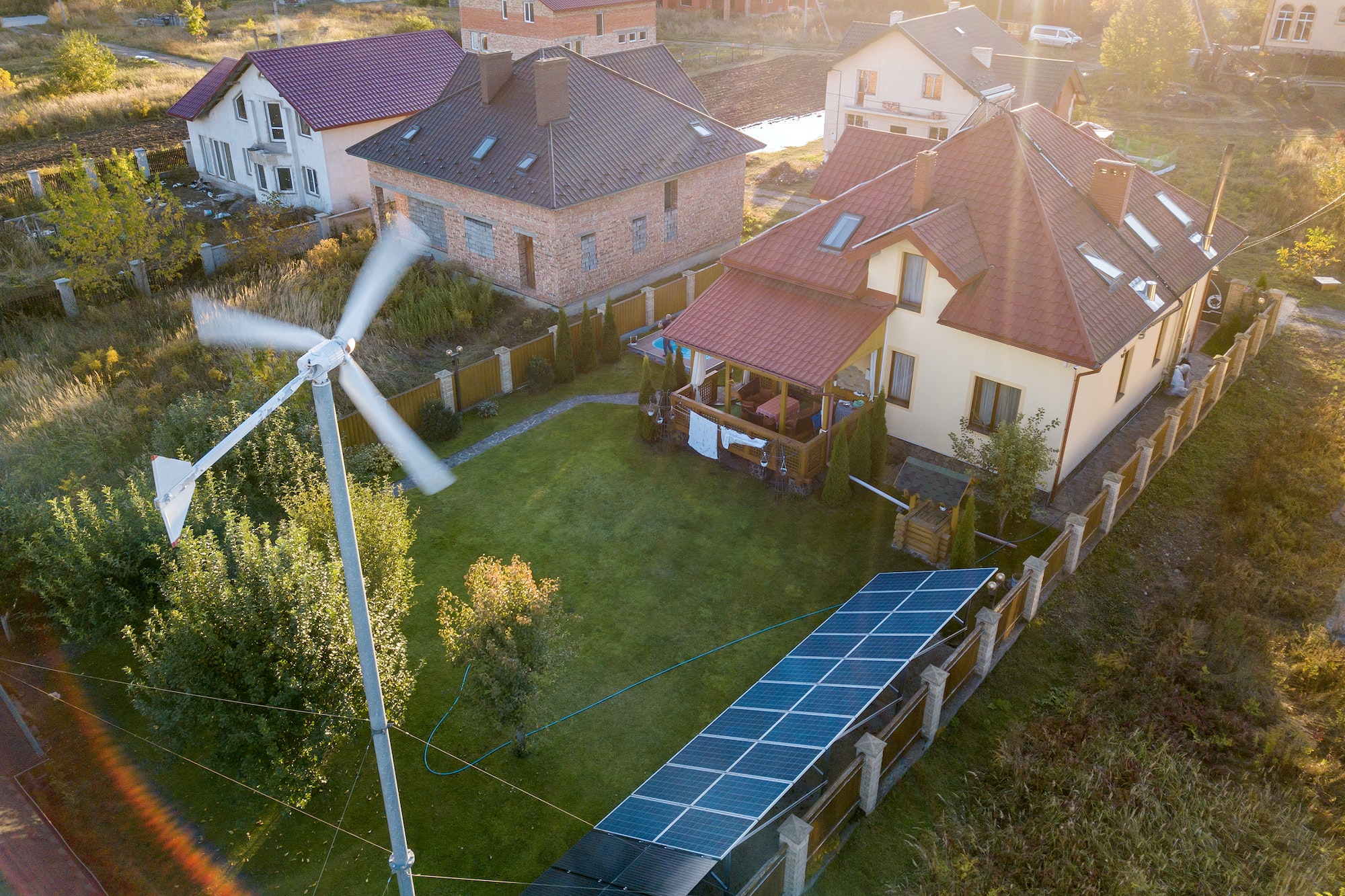 Aerial view of a residential private house with solar panels on roof and wind generator turbine