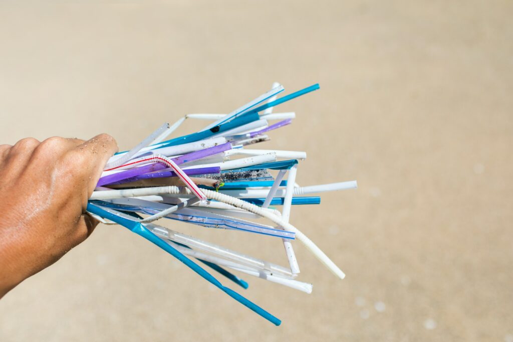 Hand holding heap of used plastic straws on background of clean beach
